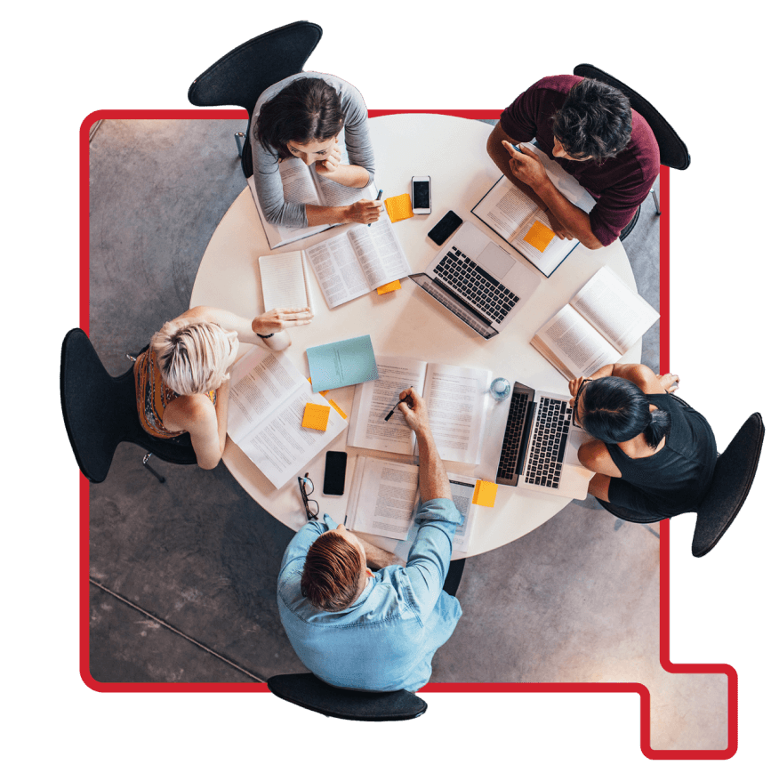 Group of five students studying together at a round table with books, laptops, and notes in a collaborative setting.